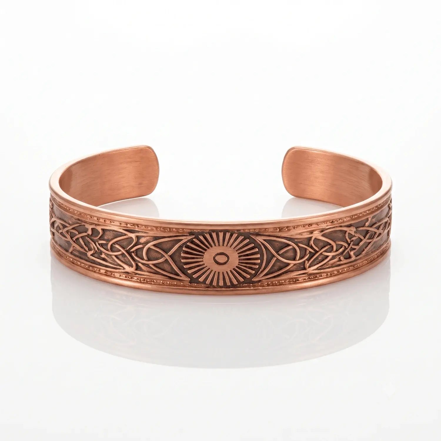 A copper-toned open cuff bracelet with engraved Celtic knotwork patterns and a central sunburst motif, displayed on a clean white reflective surface.